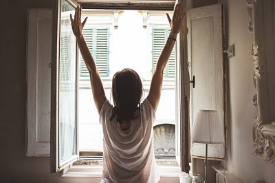 Una dona d'esquenes a la càmera fa estiraments de braços davant una finestra oberta