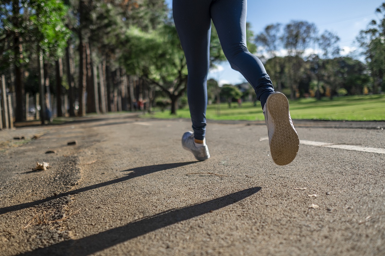 Imatge en contrapicat de les cames d'una noia que va corrent a un parc. Porta malles blaves i sabatilles de running blanques